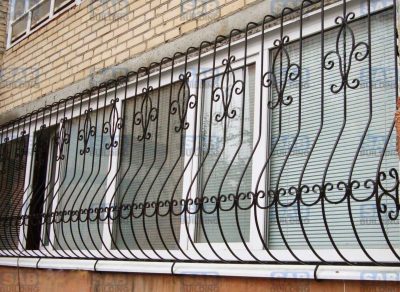 Кованые решетки на балкон Существует множество преимуществ проживания на первом этаже многоэтажного дома, но в этом случаи необходимо более ответственно подойти к защите своего жилья, устанавливая надежные решетки на окна. Особого внимания к себе требует балкон. В отличие от обычных окон, решетки на балкон требуют особого подхода, например - изменение дизайна решетки или специфическое крепление рамки. Выбор дизайна Выглядывая в окно, человек не должен ощущать себя пленником собственной квартиры. Таким образом, что бы добиться эстетически привлекательного внешнего вида, многие покупатели приобретают кованые решетки на балкон. В производстве таких решеток обычно используются кованые элементы, предавая изделию более изысканный вид. Выбирая понравившуюся модель на нашем сайте, вы можете заказать ее под любой диаметр оконного проема. Наши специалисты произведут замеры и адаптируют конструкцию даже под самые нестандартные окна. Это особенно актуально в случаи с балконом. Взять, к примеру, модель «Солнышко», будет не очень красиво, если каждая новая секция изделия будет повторять однообразный дизайн. Для достижения более привлекательного вида, будет правильно развернуть одну решетку так, что бы предать узору симметричный внешний вид. В прочем, будет проще выбрать конструкцию с однотипным дизайном, например «Тростник» или «Барашек». Сварные и кованые решетки на балкон Оба вида решеток скрепляются при помощи сварки, различие лишь в том, что в кованых решетках для балкона используют декоративные элементы, изготовленные при помощи ковки. Обычно кованые элементы представляют собой: различные завитки, листики, гроздья винограда, еловые шишки и т. д. Стоимость решеток на балкон Чем больше оконный проем, тем выше стоимость изделия, не говоря уже про оплату установки. Особенно высокой цены могут достигать кованые решетки на балкон. Что бы хоть как-то уменьшить ценник можно подобрать боле экономичные материалы, например использовать для изготовления конструкции 8 мм. прутки. Стоит также посмотреть в сторону решеток с более простым дизайном. Способ крепления Что бы правильно установить кованые решетки на балкон, необходимо обратится к опытным специалистам. Обычно при установке конструкции, кованное изделие крепится внутри оконного проема с помощью арматуры. Кроме того, решетки свариваются между собой. Именно от качества сварки зависит то, насколько надежно будет защищен Ваш дом.